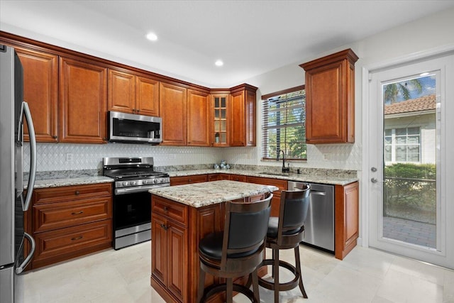 kitchen featuring sink, a kitchen island, stainless steel appliances, light stone countertops, and a kitchen bar