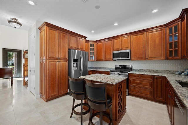 kitchen featuring a kitchen island, appliances with stainless steel finishes, a breakfast bar, decorative backsplash, and light stone counters