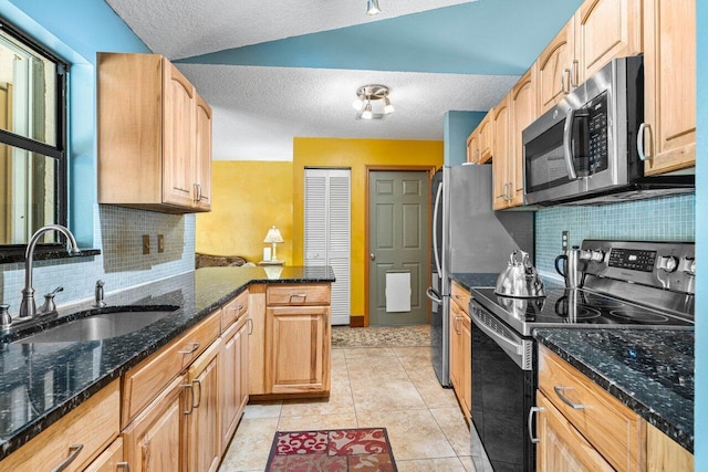 kitchen with appliances with stainless steel finishes, sink, dark stone counters, light tile patterned floors, and kitchen peninsula