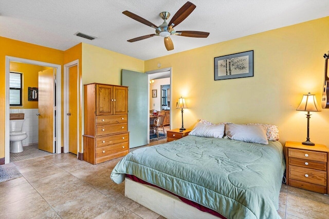 bedroom with ceiling fan, tile walls, connected bathroom, a textured ceiling, and light tile patterned flooring