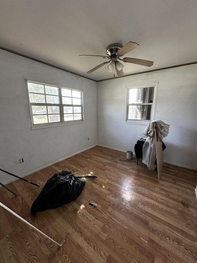 empty room featuring baseboards, crown molding, a ceiling fan, and wood finished floors