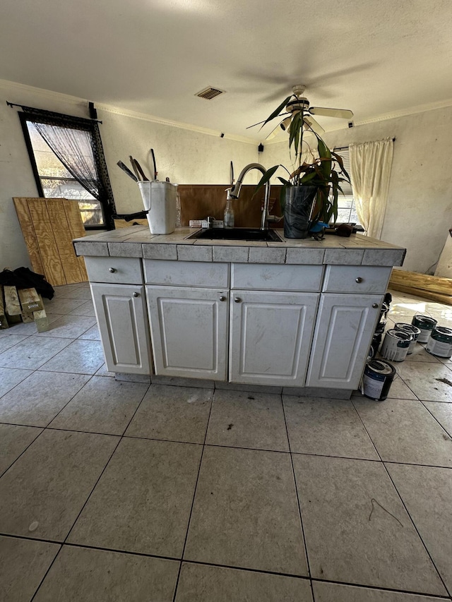 kitchen featuring light tile patterned floors, white cabinets, crown molding, and a sink