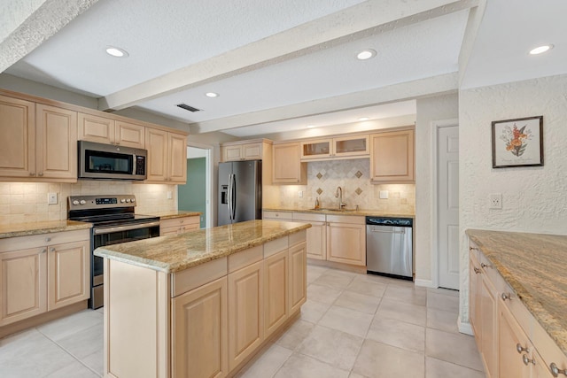 kitchen featuring beam ceiling, stainless steel appliances, a center island, light stone countertops, and light brown cabinetry