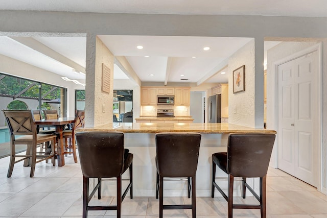 kitchen with a breakfast bar, stainless steel appliances, kitchen peninsula, and light stone countertops