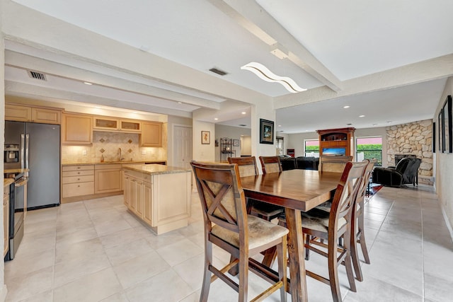 dining room featuring a stone fireplace, sink, beam ceiling, and light tile patterned floors