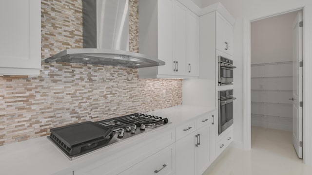 kitchen with stainless steel gas stovetop, wall chimney range hood, white cabinets, and backsplash