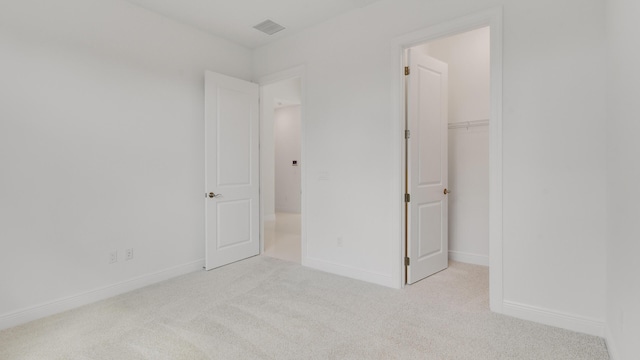 unfurnished bedroom with a walk in closet, light colored carpet, and a closet