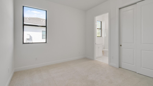 unfurnished bedroom featuring light colored carpet, a closet, and ensuite bathroom