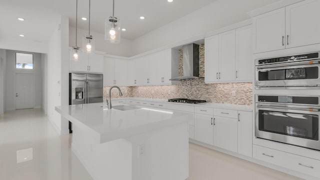 kitchen featuring sink, white cabinetry, a center island with sink, appliances with stainless steel finishes, and wall chimney range hood