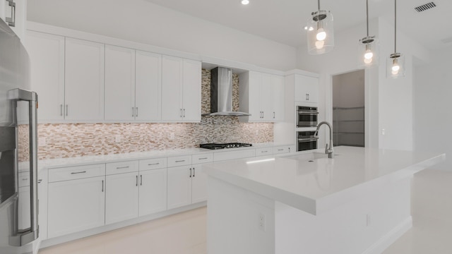 kitchen with white cabinetry, pendant lighting, stainless steel appliances, a kitchen island with sink, and wall chimney range hood