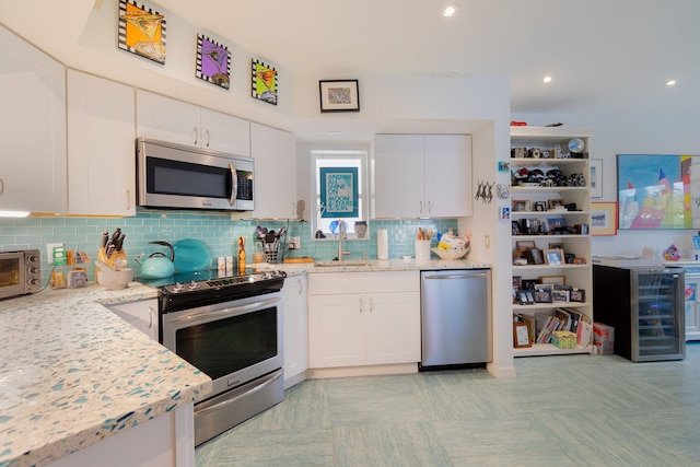 kitchen featuring sink, appliances with stainless steel finishes, white cabinetry, light stone counters, and tasteful backsplash