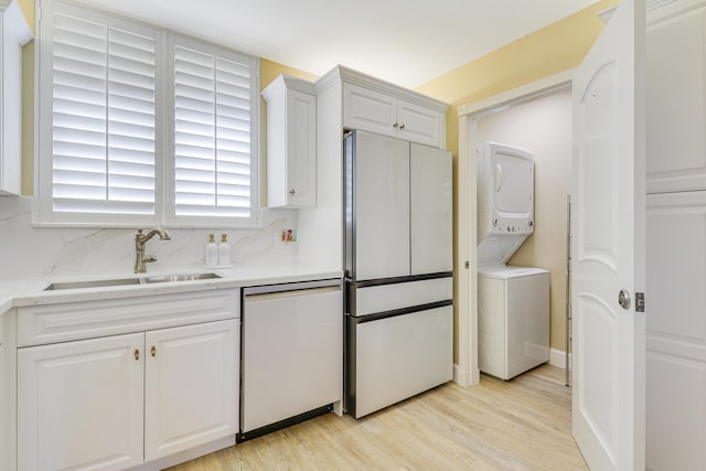 kitchen featuring dishwashing machine, sink, fridge, stacked washer / drying machine, and white cabinets