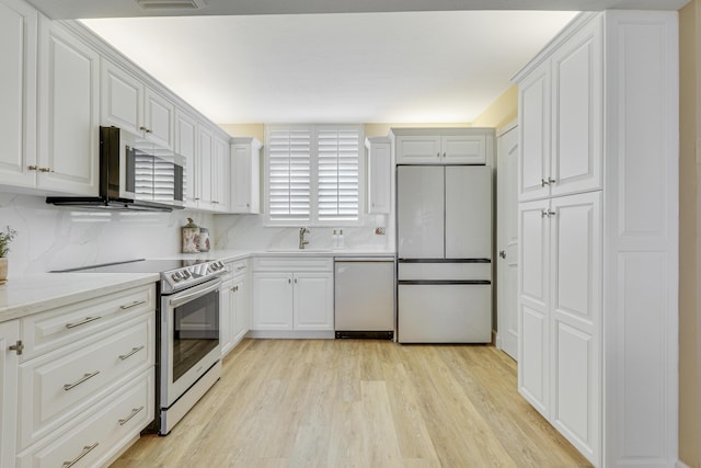 kitchen with sink, light hardwood / wood-style flooring, stainless steel appliances, tasteful backsplash, and white cabinets