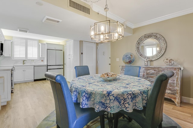 dining area with crown molding, sink, an inviting chandelier, and light wood-type flooring