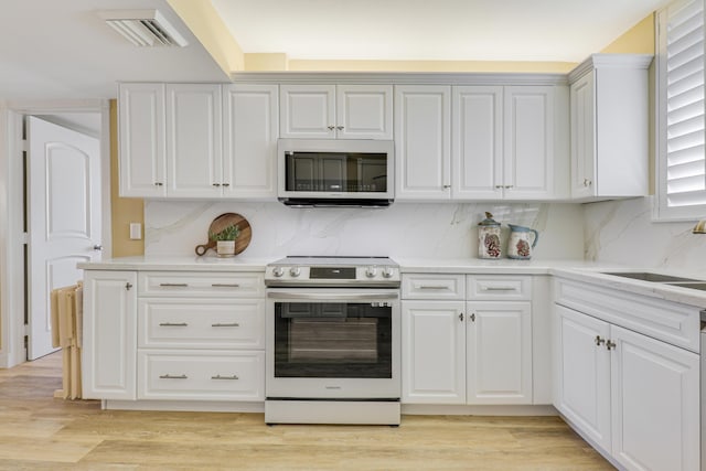 kitchen with electric stove, sink, white cabinetry, and light hardwood / wood-style floors