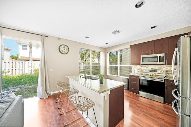 kitchen featuring backsplash, a kitchen breakfast bar, hardwood / wood-style flooring, a kitchen island with sink, and stainless steel appliances