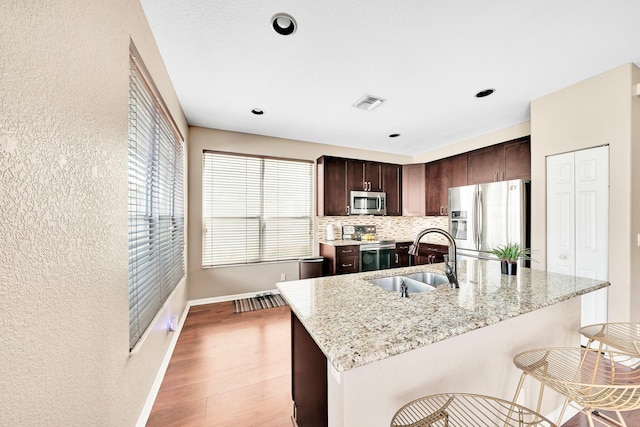 kitchen featuring sink, stainless steel appliances, light stone counters, light hardwood / wood-style floors, and an island with sink