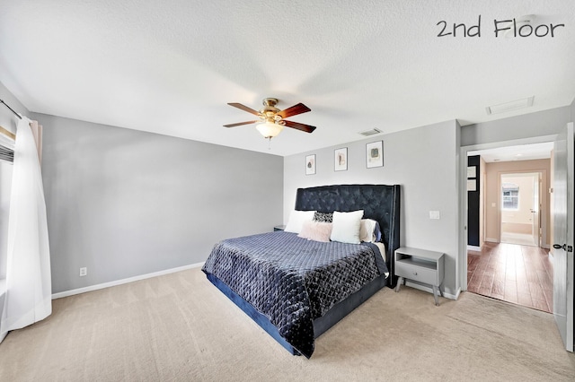 bedroom with ceiling fan, light carpet, and a textured ceiling