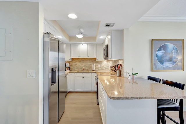 kitchen featuring a breakfast bar area, stainless steel appliances, white cabinets, decorative backsplash, and kitchen peninsula