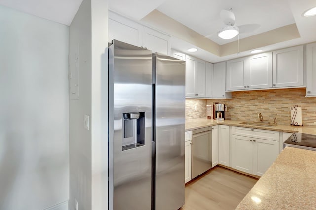 kitchen with sink, a raised ceiling, white cabinets, stainless steel appliances, and backsplash