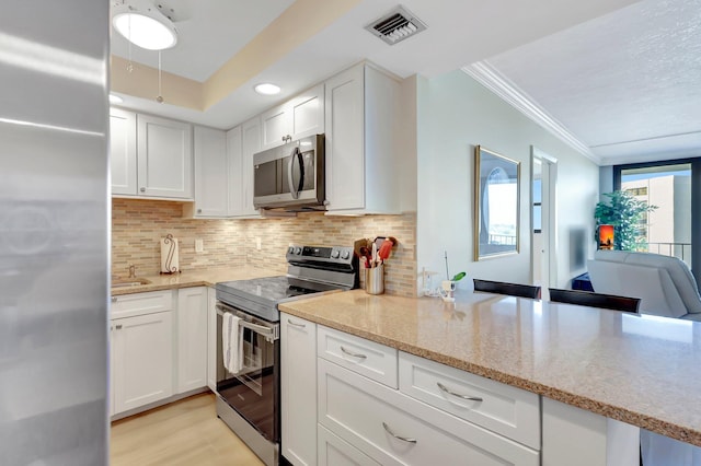 kitchen featuring white cabinetry, appliances with stainless steel finishes, crown molding, and decorative backsplash