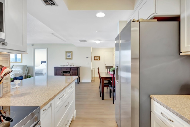 kitchen featuring white cabinetry, light stone counters, stainless steel fridge with ice dispenser, light wood-type flooring, and stove