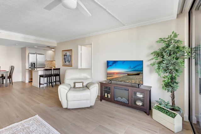 living room featuring ceiling fan, light hardwood / wood-style flooring, ornamental molding, and a textured ceiling