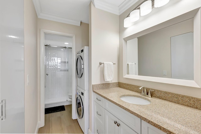 bathroom with ornamental molding, stacked washer / dryer, toilet, and a tile shower