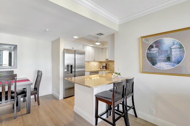 kitchen featuring a breakfast bar area, backsplash, stainless steel appliances, white cabinets, and kitchen peninsula