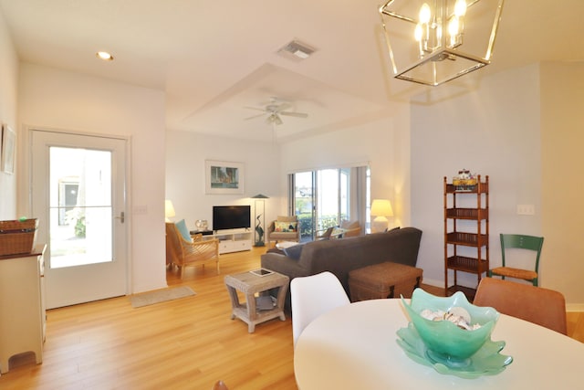 living room featuring ceiling fan with notable chandelier and light wood-type flooring