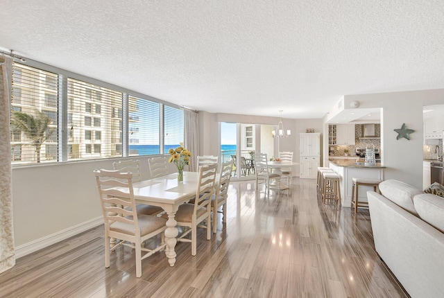 dining room with a water view, a textured ceiling, a notable chandelier, and light wood-type flooring