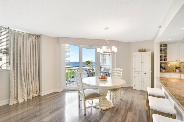 dining room with a water view, an inviting chandelier, a textured ceiling, and light wood-type flooring