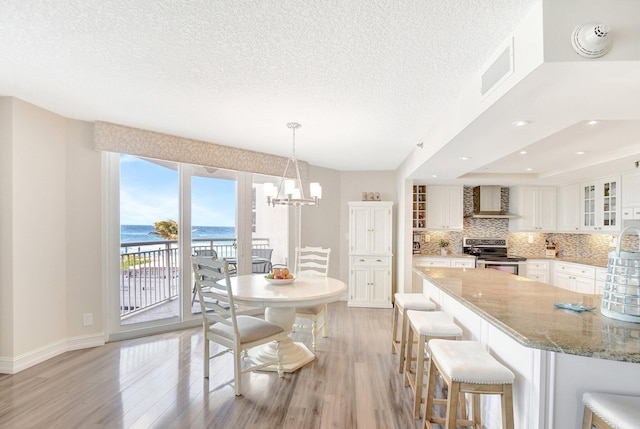 kitchen with tasteful backsplash, white cabinets, stainless steel range with electric stovetop, a water view, and wall chimney exhaust hood