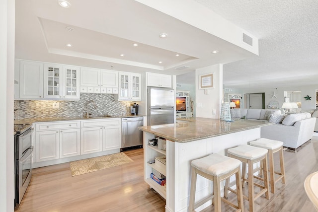 kitchen featuring white cabinetry, sink, a breakfast bar area, a tray ceiling, and stainless steel appliances