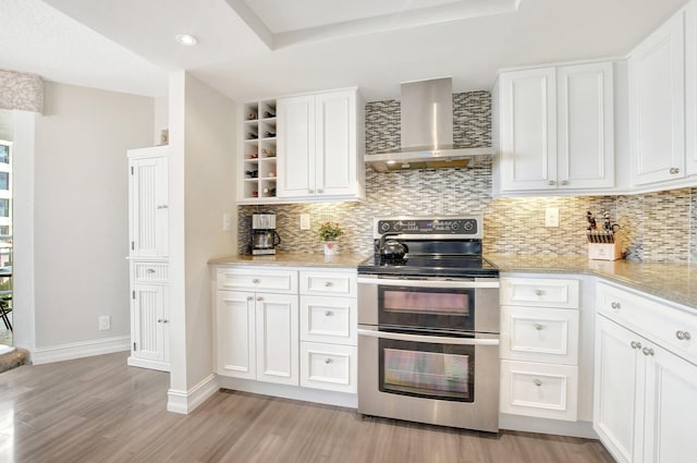 kitchen with white cabinetry, wall chimney exhaust hood, range with two ovens, and light wood-type flooring