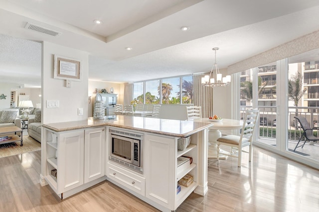 kitchen featuring pendant lighting, stainless steel microwave, light stone counters, white cabinets, and kitchen peninsula