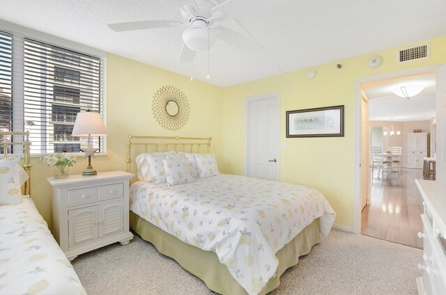 bedroom with light carpet and ceiling fan with notable chandelier