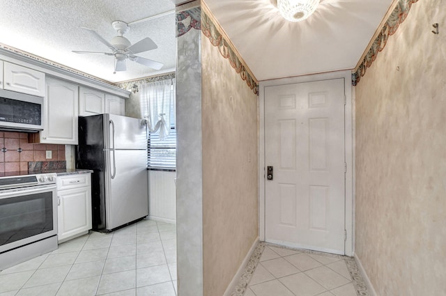 kitchen featuring light tile patterned flooring, appliances with stainless steel finishes, white cabinetry, decorative backsplash, and a textured ceiling