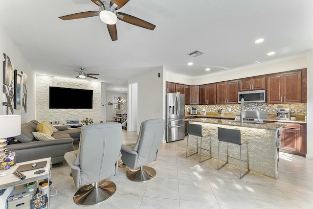 kitchen with an island with sink, backsplash, a kitchen breakfast bar, light stone counters, and stainless steel appliances