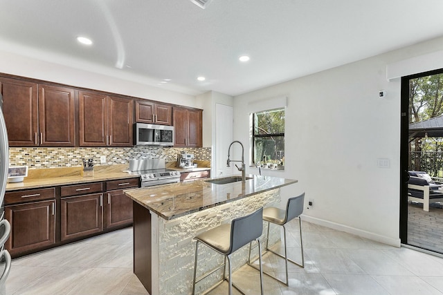 kitchen with sink, a kitchen island with sink, stainless steel appliances, a kitchen bar, and decorative backsplash