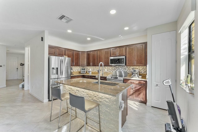 kitchen with a breakfast bar area, stainless steel appliances, light stone counters, tasteful backsplash, and a center island with sink