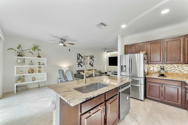 kitchen featuring sink, tasteful backsplash, an island with sink, stainless steel appliances, and light stone countertops