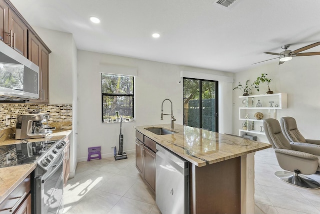 kitchen featuring light tile patterned flooring, sink, stainless steel appliances, a kitchen island with sink, and decorative backsplash