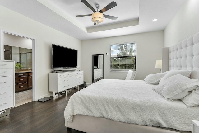 bedroom with ceiling fan, connected bathroom, a tray ceiling, and dark hardwood / wood-style flooring