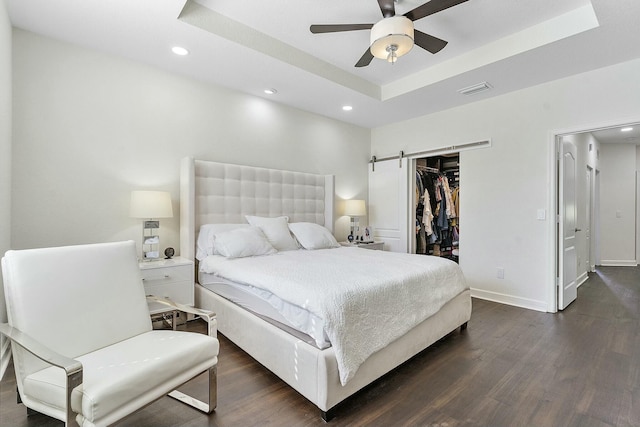 bedroom featuring dark wood-type flooring, a walk in closet, a tray ceiling, a closet, and a barn door