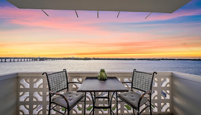 balcony at dusk featuring a water view