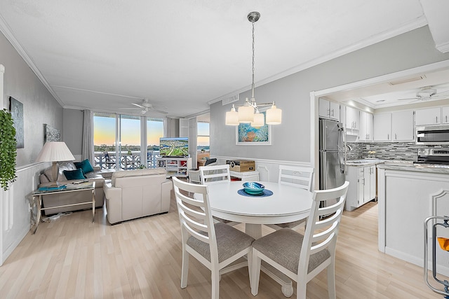 dining room featuring light wood-type flooring, wainscoting, crown molding, and ceiling fan with notable chandelier