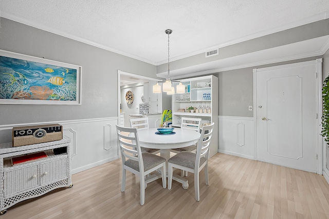 dining room featuring a textured ceiling, light wood-style floors, visible vents, and ornamental molding