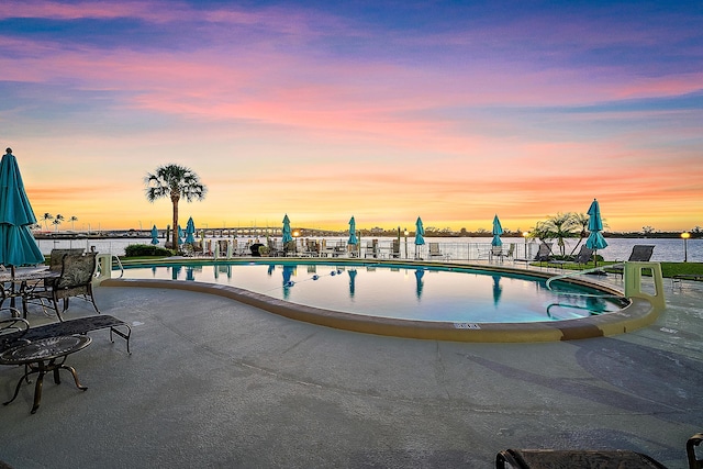 pool at dusk with a patio, fence, and a community pool