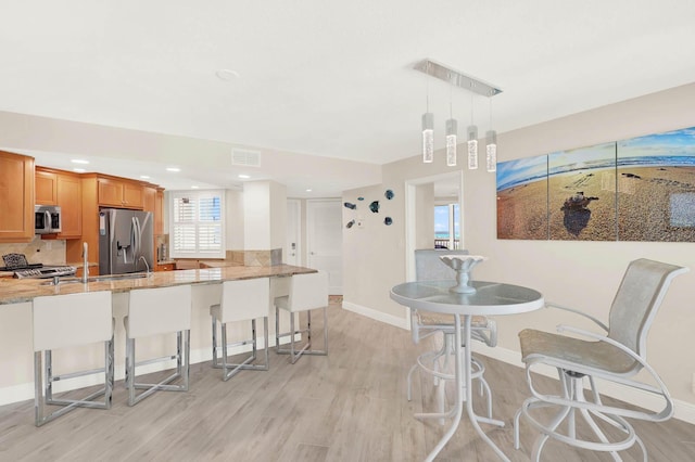 kitchen featuring hanging light fixtures, stainless steel appliances, light stone countertops, kitchen peninsula, and light wood-type flooring